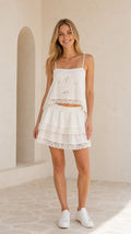 Model wearing white embroidered cami top and tiered lace mini skirt two-piece set front view