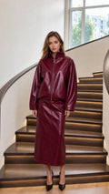 Woman wearing burgundy glossy faux leather jacket and midi skirt set on stairs front view