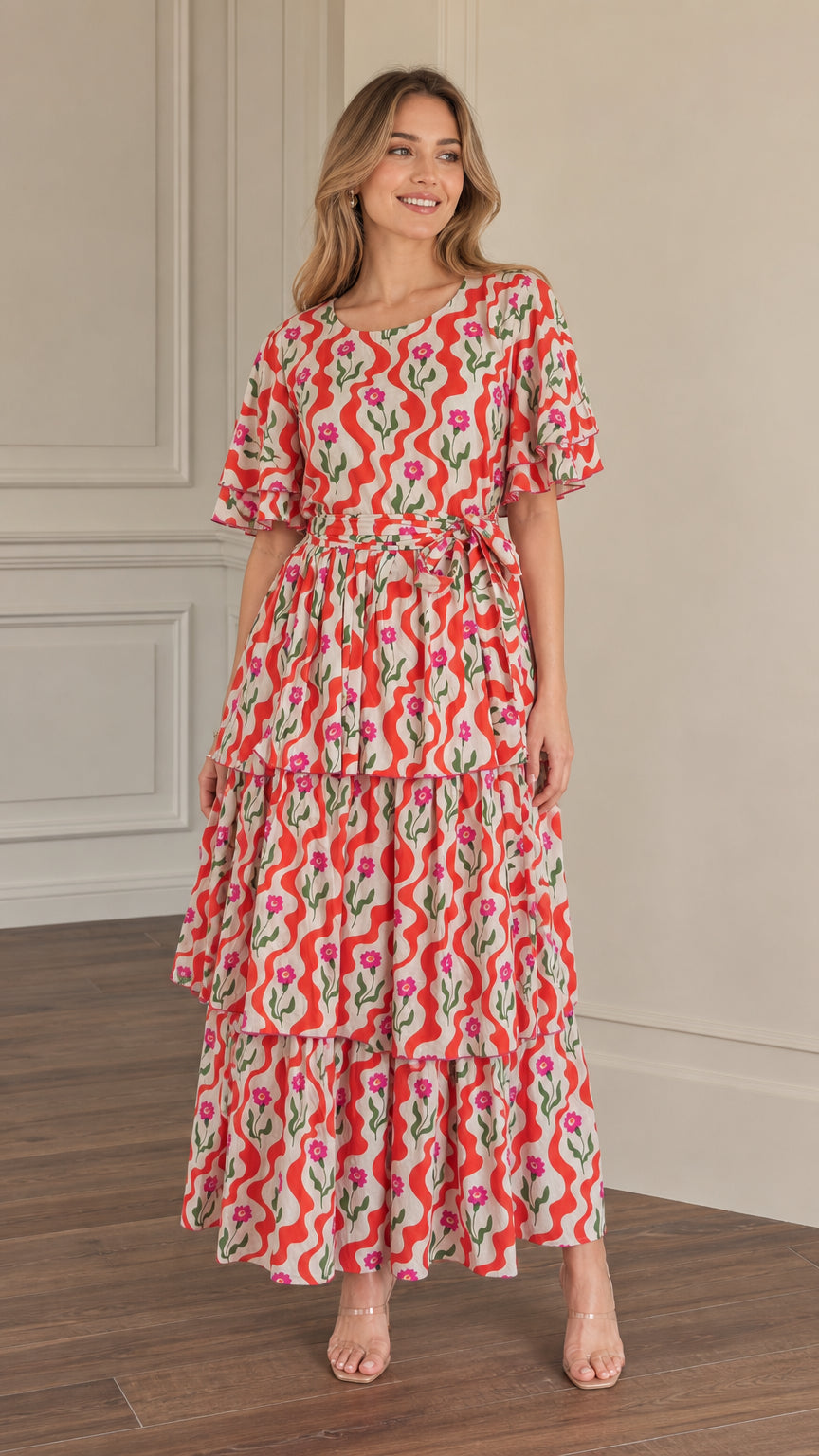 Front full-length view of woman wearing red floral wave print tiered maxi dress with tie waist