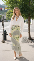 Full front view of model wearing pale yellow floral midi skirt with grey fringe trims and white shirt