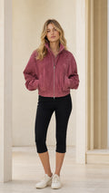 Front view of woman wearing rose pink full-zip bomber jacket with black capris and sneakers