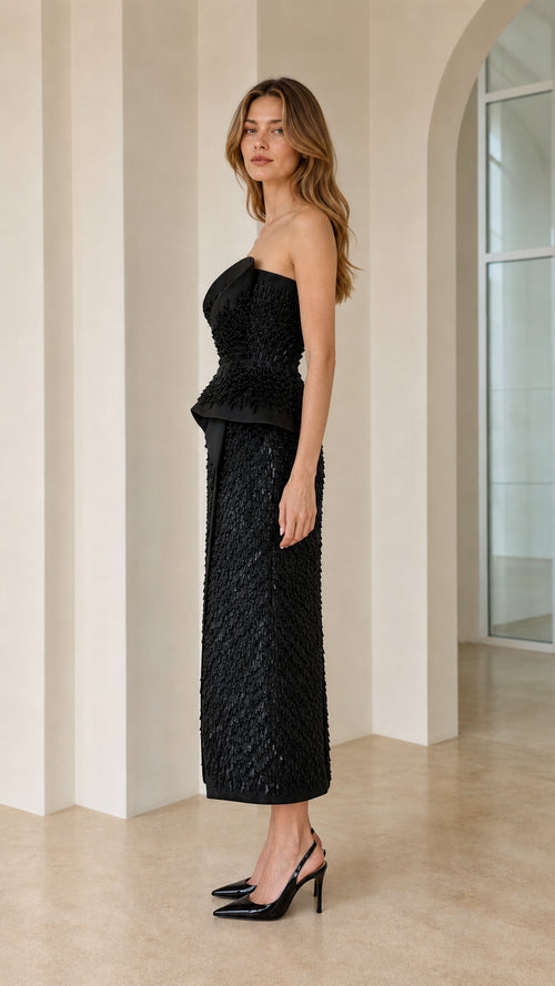 Side profile view of black strapless dress with peplum waist