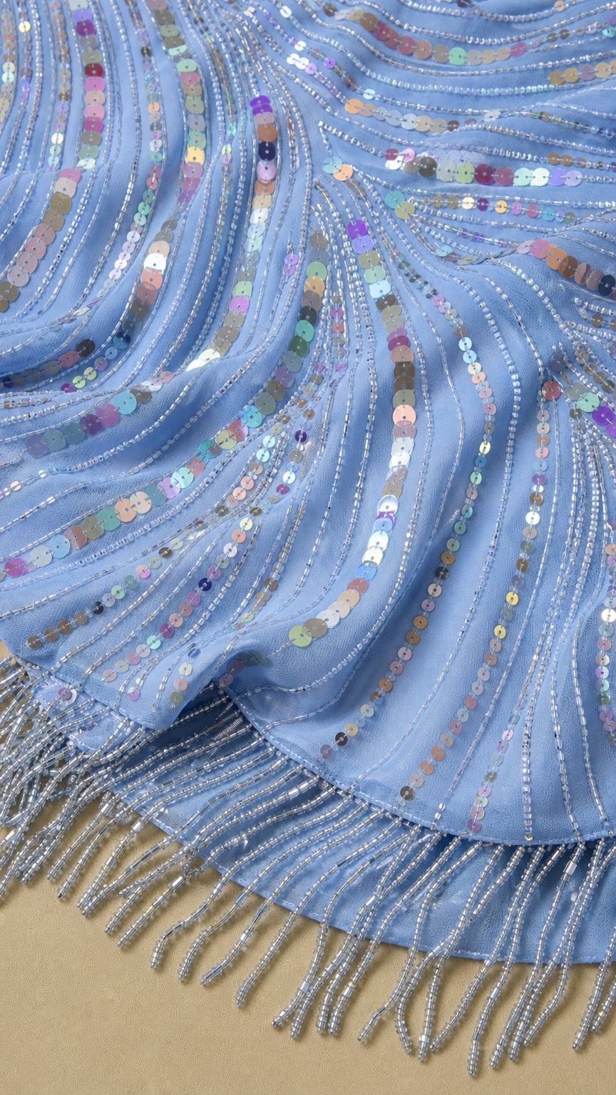 Close-up of iridescent sequins, beadwork, and tassel fringe on light blue fabric