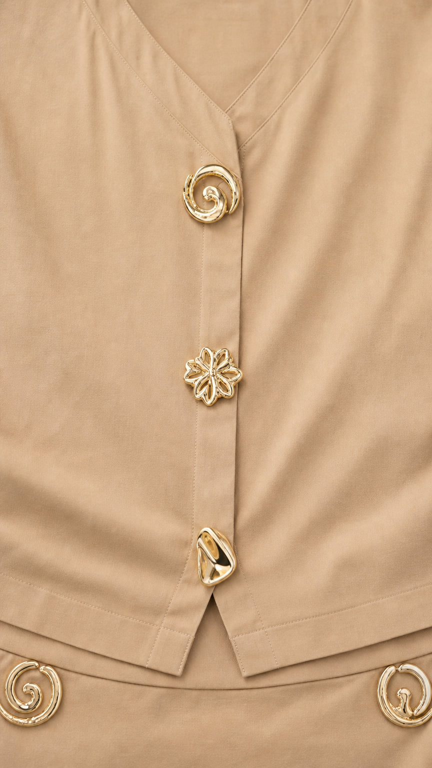 Close-up detail of sculptural gold-tone buttons on khaki V-neck blouse and waistband