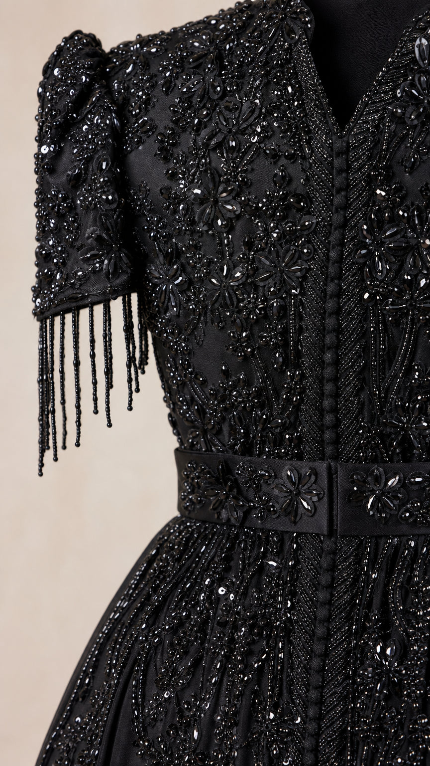 Close-up detail of the black gown bodice showing intricate beadwork, sequins, and sleeve fringe