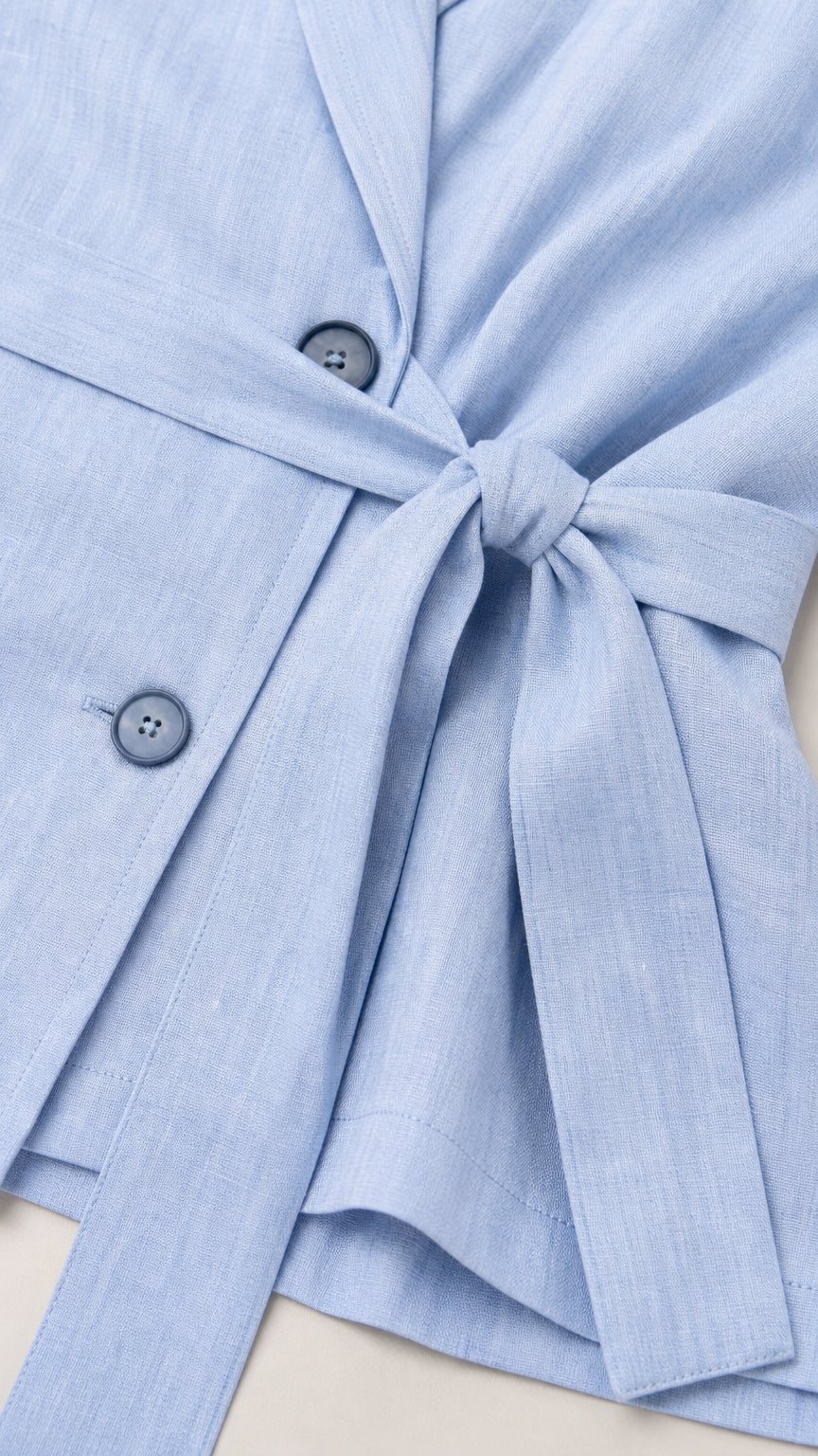 Close-up detail of light blue blazer buttons and self-tie belt