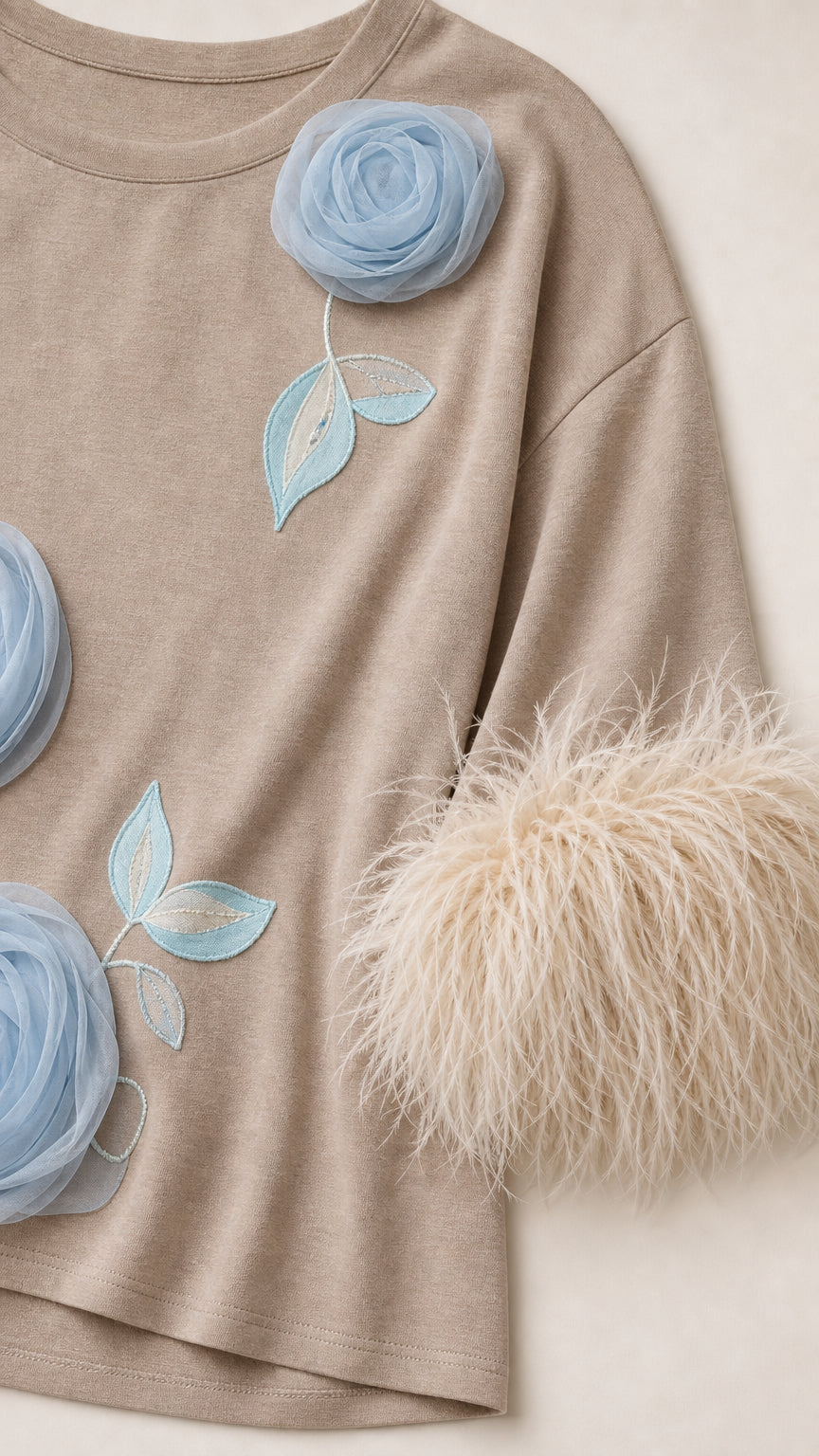 Close-up detail of blue floral appliques and feather cuffs on beige top