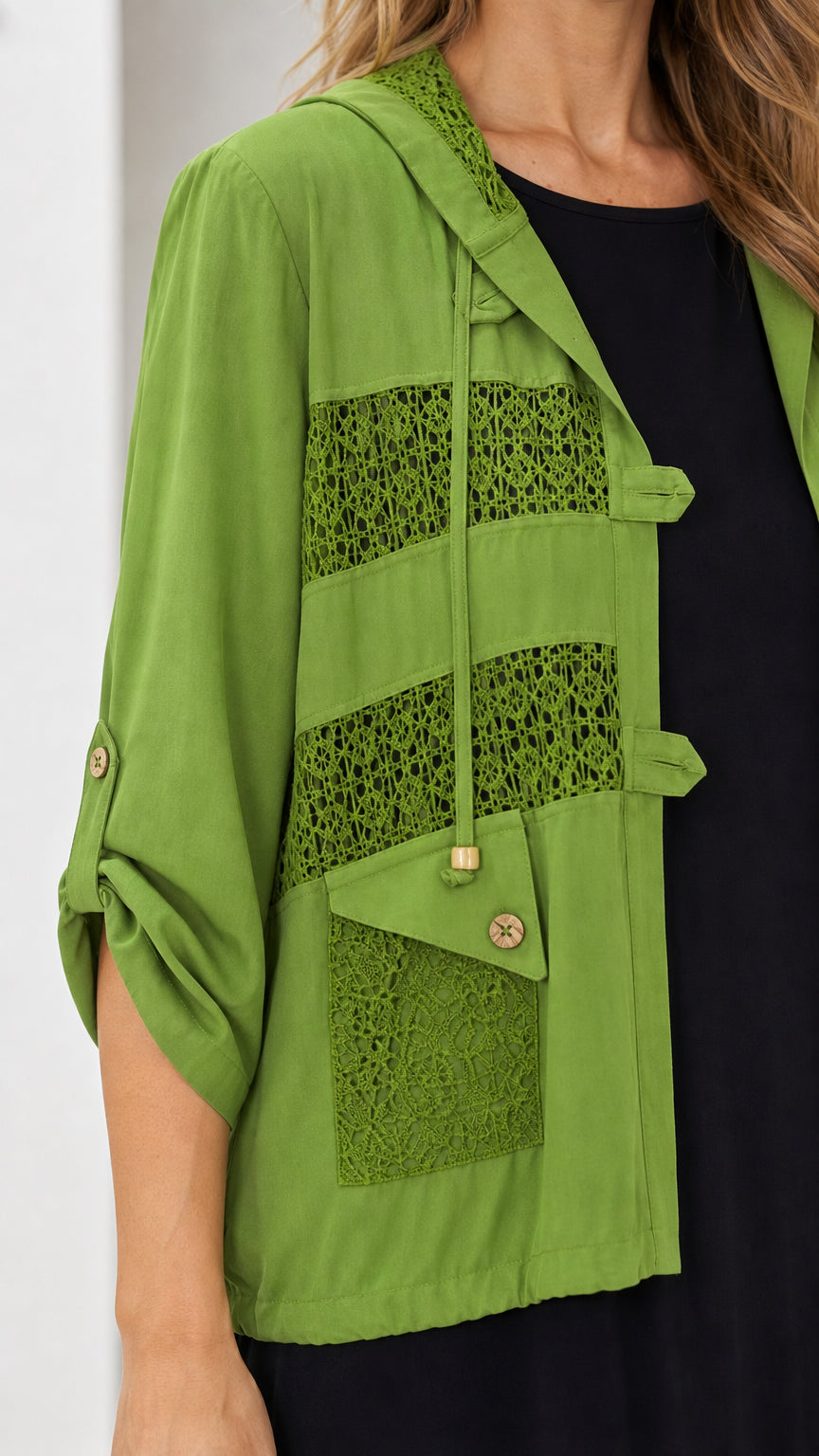Close-up detail of olive green jacket showcasing crochet lace panels, pocket, and hood drawstrings