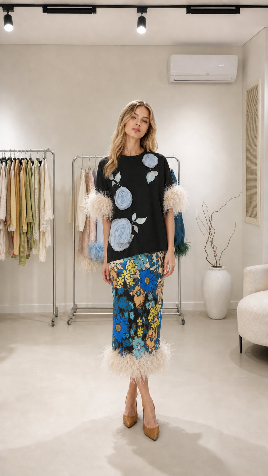 Model wearing black two-piece set with floral appliques and feather trim